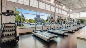 A gym with treadmills, a stair climber, and a large window with a view of the outside. - Sea Colony Ocean 7th floor condo w/ gym, balcony, and tennis court (Bethany Beach)