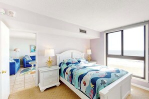 Un dormitorio con cama, mesitas de noche, una ventana con vistas y una puerta que da a otra habitación.