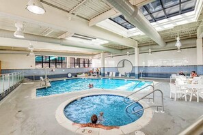 Una piscina cubierta con varias pistas, un jacuzzi y un área soleada con mesas y sillas.