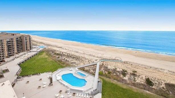 A hotel with a pool, beach view, and a large building in the background. - Sea Colony Ocean 14th floor condo w/ tennis court, shared sauna, and free WiFi (Bethany Beach)