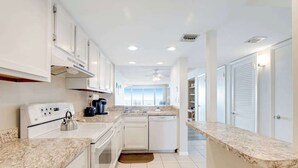 A modern kitchen with white cabinetry, a built-in oven, a coffee maker, and a dishwasher. - Sea Colony Ocean 14th floor condo w/ tennis court, shared sauna, and free WiFi (Bethany Beach)