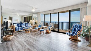 A spacious living area with a balcony, wicker furniture, and a large window offering a view. - Sea Colony Ocean 14th floor condo w/ tennis court, shared sauna, and free WiFi (Bethany Beach)