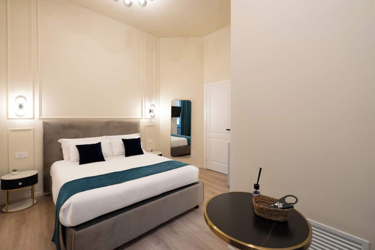 A modern hotel room with a large bed, bedside tables, a round table, and a mirror.