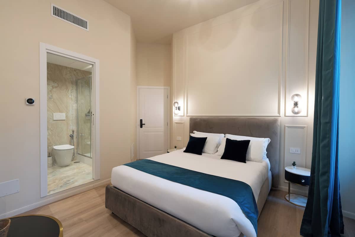 A bedroom with a bed, bedside tables, a nightstand, a mirror, and a door leading to a bathroom.