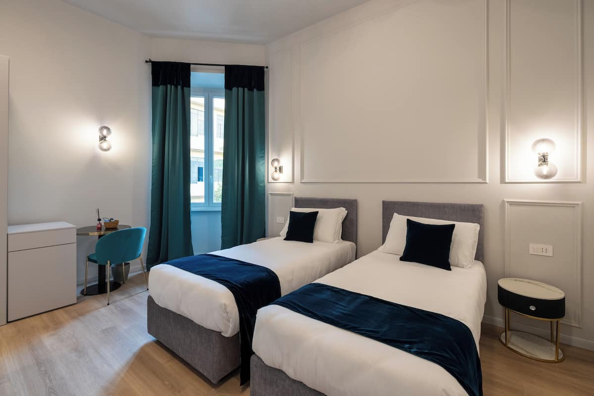 A hotel room with two beds, a desk, a chair, and a round side table.