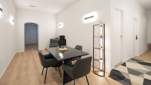 Un espace repas moderne avec une table noire, quatre chaises, une petite étagère ornée d’objets décoratifs et une porte en arrière-plan.