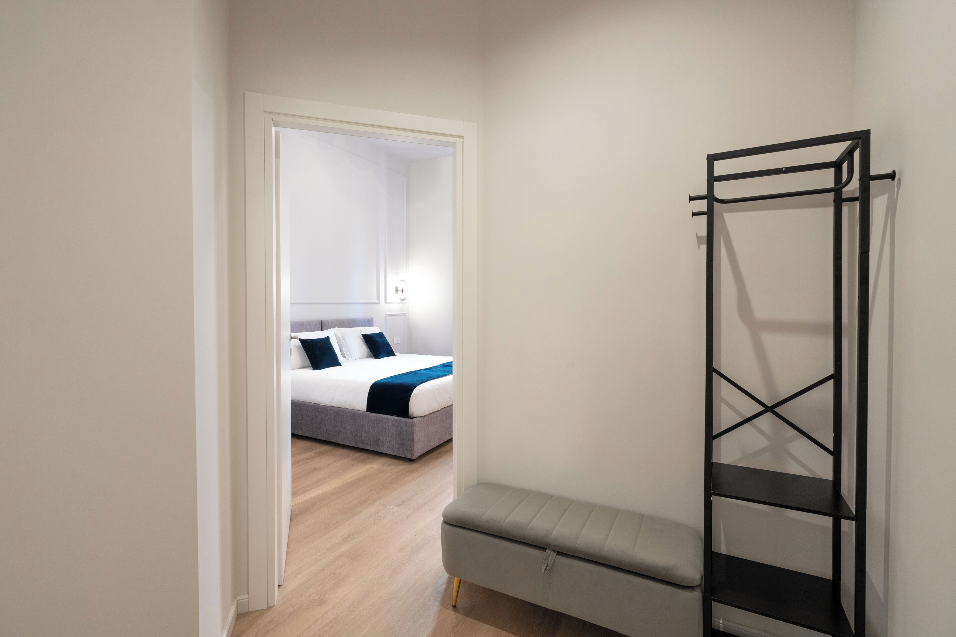 A bedroom with a bed, a bench, and a black metal shelf unit.