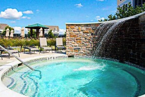 A hot tub with a stone wall and a waterfall feature, surrounded by lounge chairs and umbrellas. - Dog-friendly resort townhouse w/shared sauna, fireplace, basketball/tennis court (Selbyville)