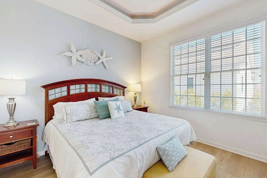 A bedroom with a large bed, a nightstand, a lamp, a starfish wall decoration, and a window with blinds.