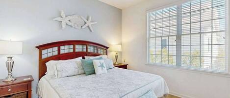 A bedroom with a large bed, a nightstand, a lamp, a starfish wall decoration, and a window with blinds.