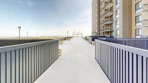 Un long chemin rectiligne menant à un bâtiment doté de nombreux balcons, un ciel dégagé et une vue lointaine sur la plage.
