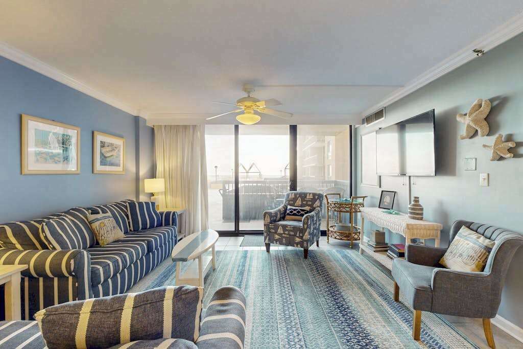 Ein Wohnzimmer mit einer Couch, Sesseln, einem Couchtisch, einem Fernseher und einem Balkon mit Blick.