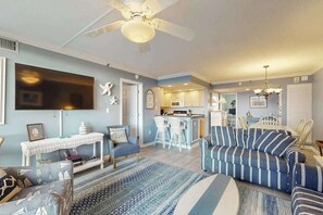 A living room with a sofa, chairs, a TV, a ceiling fan, and a kitchen area. - Sea Colony Ocean 1st floor condo w/ balcony, free WiFi, and shared sauna (Bethany Beach)