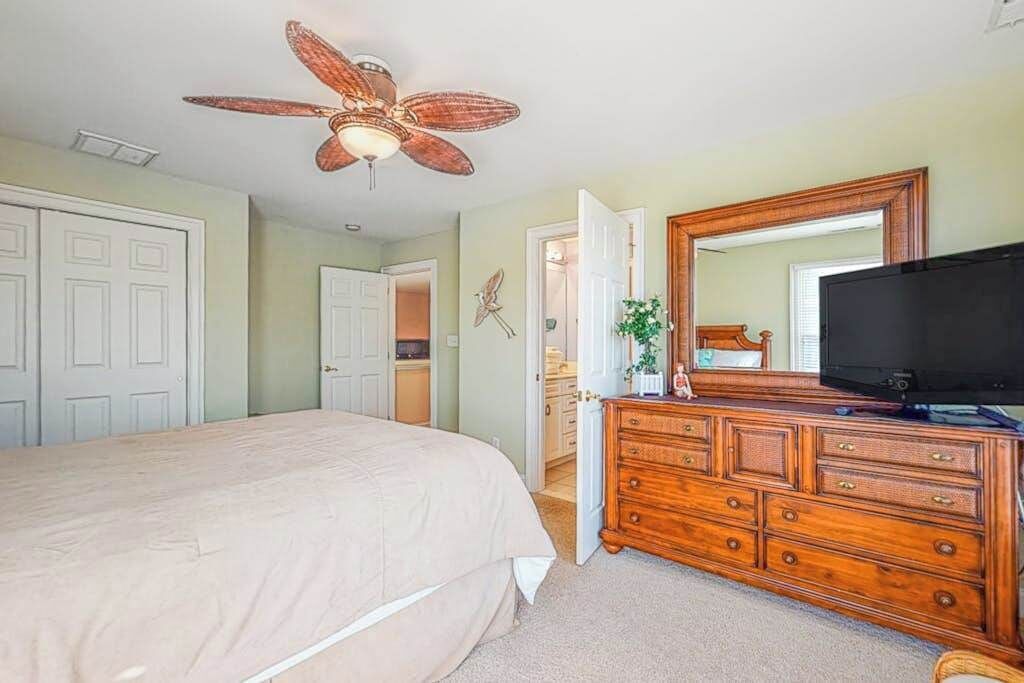 Ein Schlafzimmer mit einem Bett, einer Holzkommode, einem Deckenventilator, einem großen Spiegel und einem Fernseher.