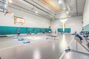 Ein Fitnessstudio mit Basketballkorb, Trainingsgeräten und einem großen Spiegel.
