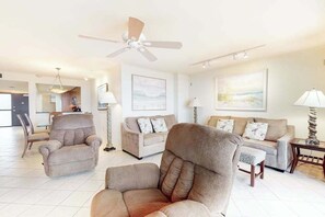 Ein geräumiges Wohnzimmer mit Deckenventilator, zwei Sofas, einem Sessel und einer Lampe.