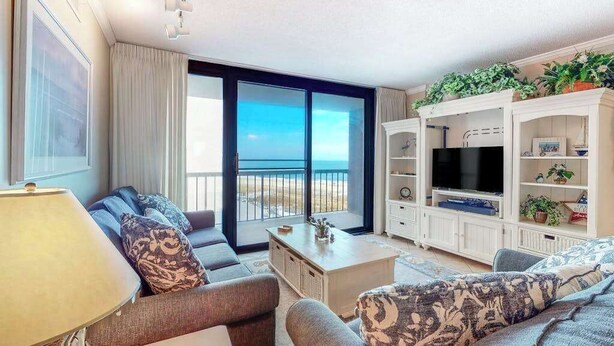 Een woonkamer met een bank, een salontafel, een tv-meubel en uitzicht op het strand.