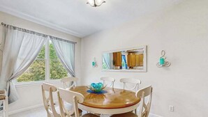 Un comedor con una mesa redonda, sillas, una lámpara de araña y una ventana con cortinas.