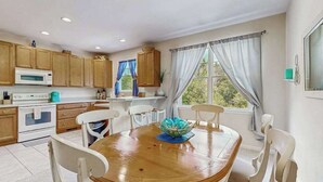 Una cocina con armarios de madera, un microondas, una mesa de comedor con sillas y una ventana con cortinas.