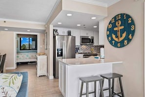 A modern kitchen with a central island, stainless steel appliances, and a large anchor-themed wall clock. - Sea Colony Ocean 5th floor condo w/ free WiFi, elevator, and balcony (Bethany Beach)