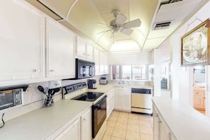 A kitchen with white cabinets, a stove, microwave, and a ceiling fan. - Sea Colony oceanfront 8th floor condo with shared sauna, tennis court, & pool (Bethany Beach)