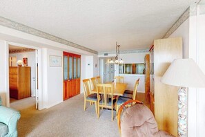 A dining area with a wooden table and chairs, a chandelier, and a lamp. - Sea Colony oceanfront 8th floor condo with shared sauna, tennis court, & pool (Bethany Beach)