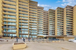 Een meerlaags hotel met balkons, een overdekt buitengebied en een parkeerplaats.