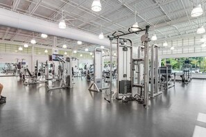 Een ruime fitnessruimte met diverse trainingsapparaten, grote ramen en een hoge plafond.