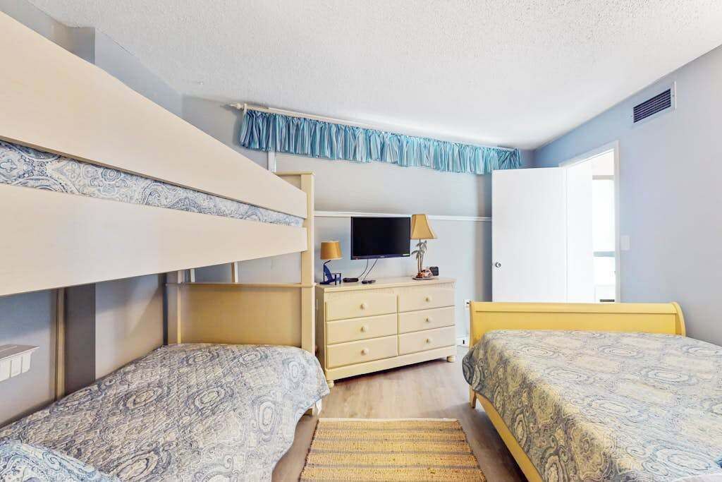 A bedroom with bunk beds, a television, a dresser, and a door leading to another room.