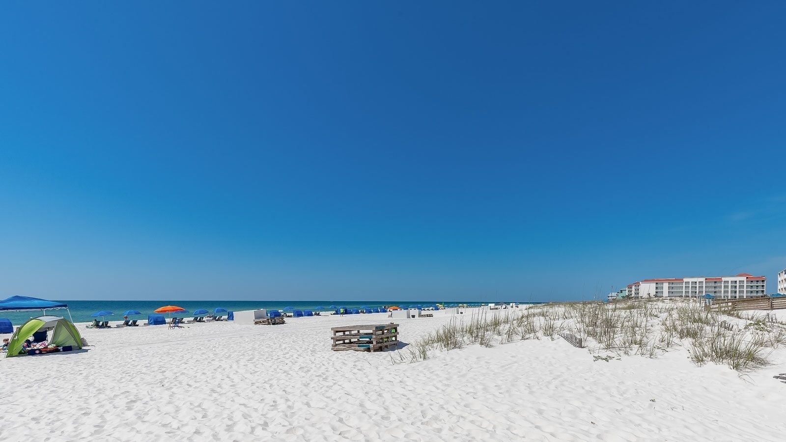 A beach with tents, umbrellas, and a wooden structure.