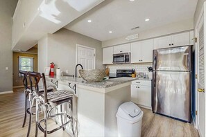 A modern kitchen with white cabinetry, stainless steel appliances, and a central island with bar stools. - Sea Colony Tennis 2nd floor condo w/shared pool, hot tub, pickleball courts, gym (Bethany Beach)