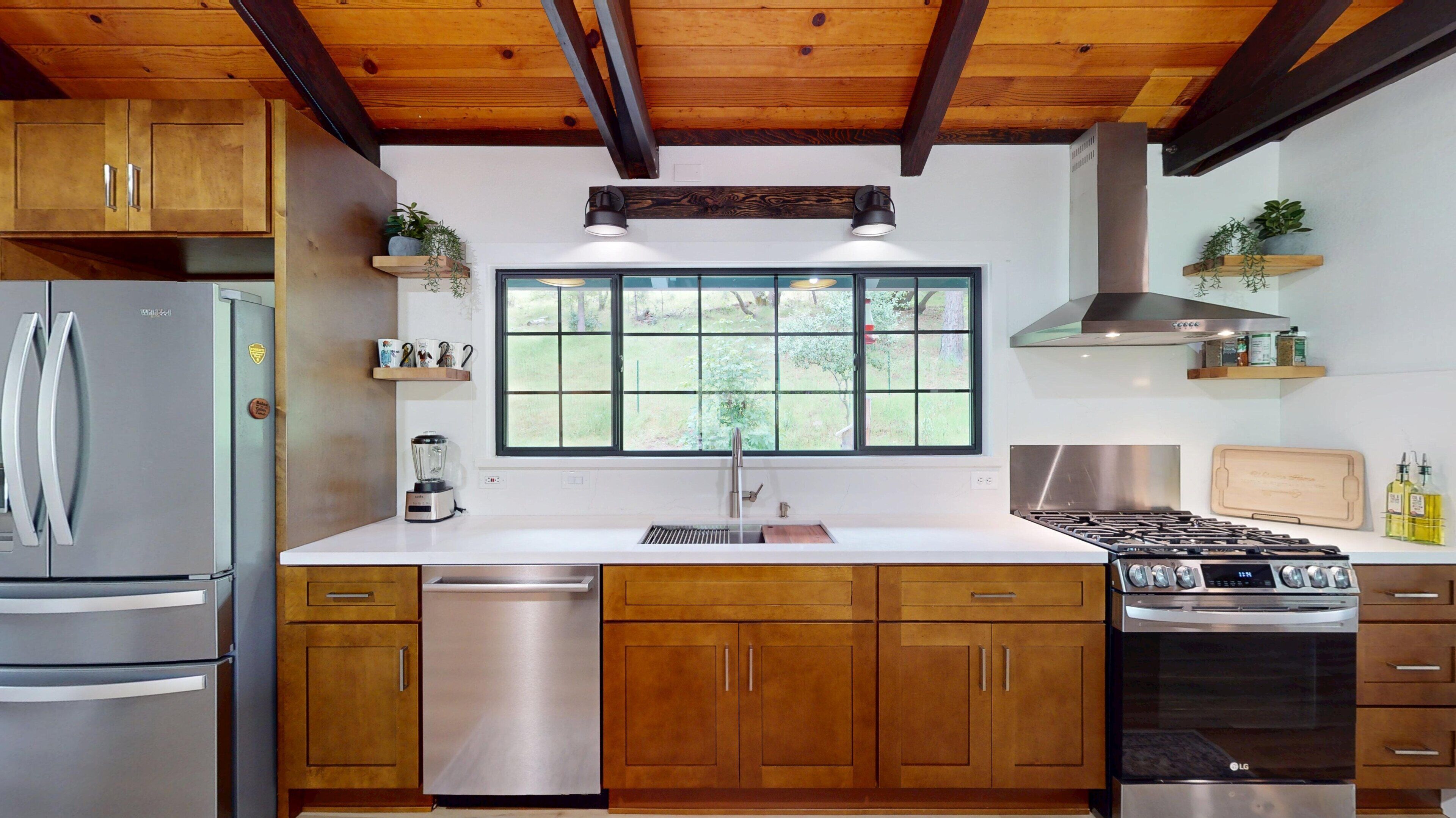 A modern kitchen with wooden cabinets, stainless steel appliances, a window with a view, and built-in shelves.