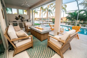 A poolside area with wooden chairs, a fire pit, and a view of a pool and palm trees. - Gulfcoast Oasis - 910 Golf Island Dr 4 Bedroom Home (Apollo Beach)
