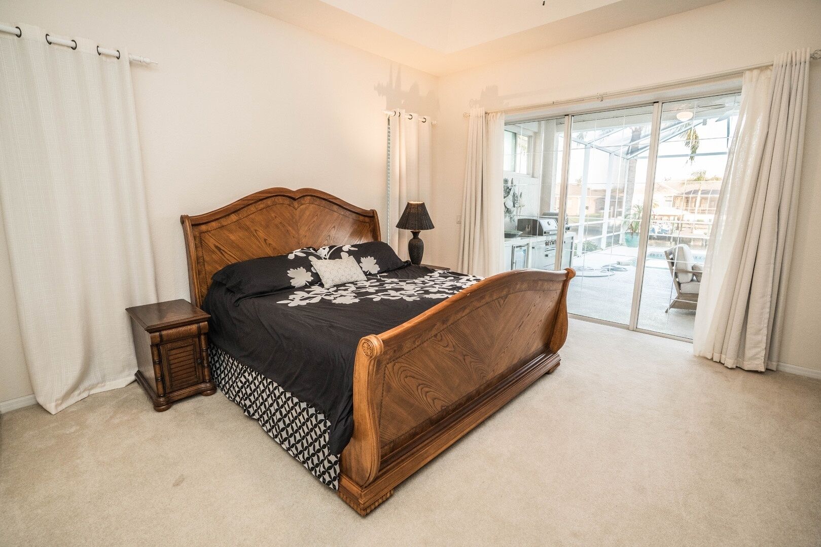 Un dormitorio con una cama de madera, una mesita de noche, una lámpara y vistas a un balcón con mobiliario exterior.