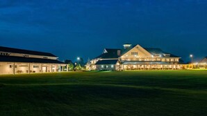A large building with multiple sections, including a prominent central building with a sloped roof and a smaller building to the left. - Bayside Resort townhouse w/ gym, private gas grill, pool, and free WiFi (Selbyville)