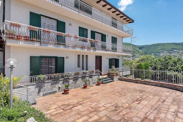 A multi-story building with balconies, potted plants, and a stone-paved courtyard. - Olympus Apartment – Agerola (Pianillo)