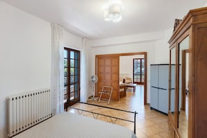 A room with a bed, a radiator, a fan, a wooden door, and a wardrobe. - Olympus Apartment – Agerola (Pianillo)