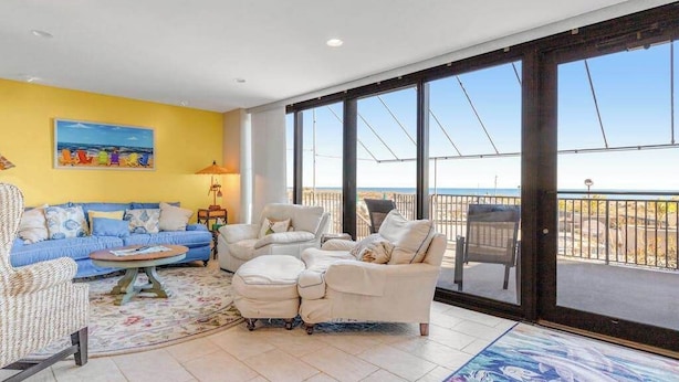 A living room with a sofa, armchairs, a coffee table, and a rug. There is a large window with a view of the beach. - Sea Colony Ocean 1st-floor condo with access to pool & tennis court, balcony (Bethany Beach)