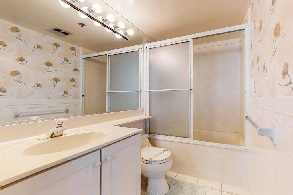 A bathroom with a toilet, a sink, a mirror, and a shower area.