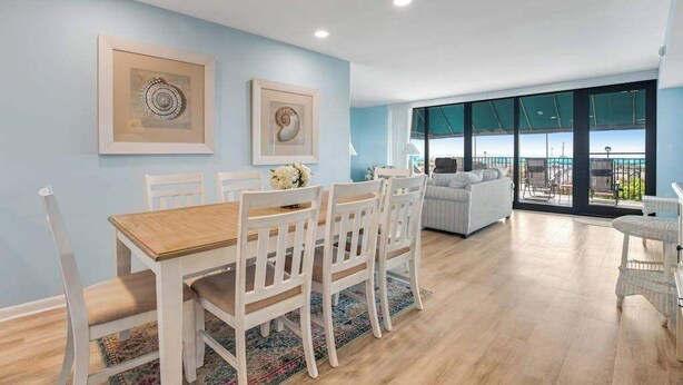 Een eetgedeelte met een houten tafel en witte stoelen, een bank en een balkon met uitzicht.