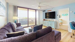 Een woonkamer met een bank, een televisie, een plafondventilator en een schuifdeur naar een buitengebied.