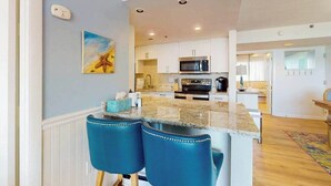 Een moderne keuken met witte kasten, een granieten aanrecht en een magnetron. Er staan twee blauwe barkrukken bij het eiland.