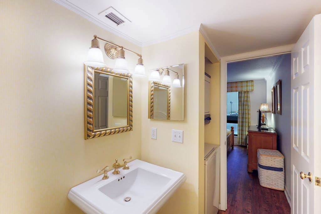 A bathroom with a white sink, two mirrors with gold frames, and a light fixture above the sink.