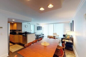 Een moderne keuken met houten kasten, een eetgedeelte met een houten tafel en stoelen, en een woonruimte met een bank en een televisie.