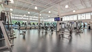 Een ruime fitnessruimte met diverse trainingsapparaten, grote ramen en een hoge plafond.
