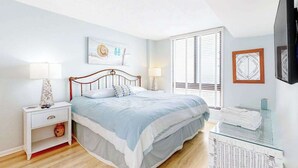 Een slaapkamer met een bed, nachtkastjes, een televisie en een glazen tafel met handdoeken.