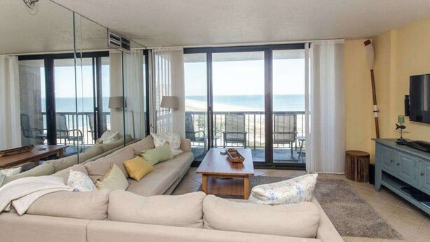 A modern living room with a sofa, coffee table, and a view of the sea through large windows. - Sea Colony oceanfront, 7th-floor condo w/ pool and ocean view (Bethany Beach)