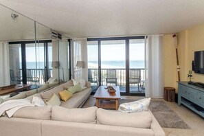 A modern living room with a sofa, coffee table, and a view of the sea through large windows. - Sea Colony oceanfront, 7th-floor condo w/ pool and ocean view (Bethany Beach)