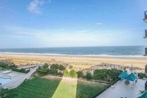 A view of a beach with a clear sky, a pool area, and a building with a balcony overlooking the ocean. - Sea Colony oceanfront, 7th-floor condo w/ pool and ocean view (Bethany Beach)