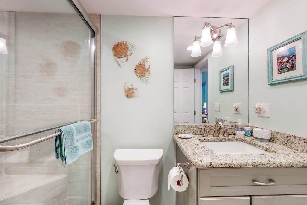 Ein Badezimmer mit Duschkabine aus Glas, Toilette, Waschbecken mit Granitplatte und Wandleuchten.